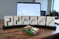 Soporte Oliver Velez con seis cartas de My Trading Poker de pie sobre un escritorio de nogal, frente a un portátil con un gráfico.